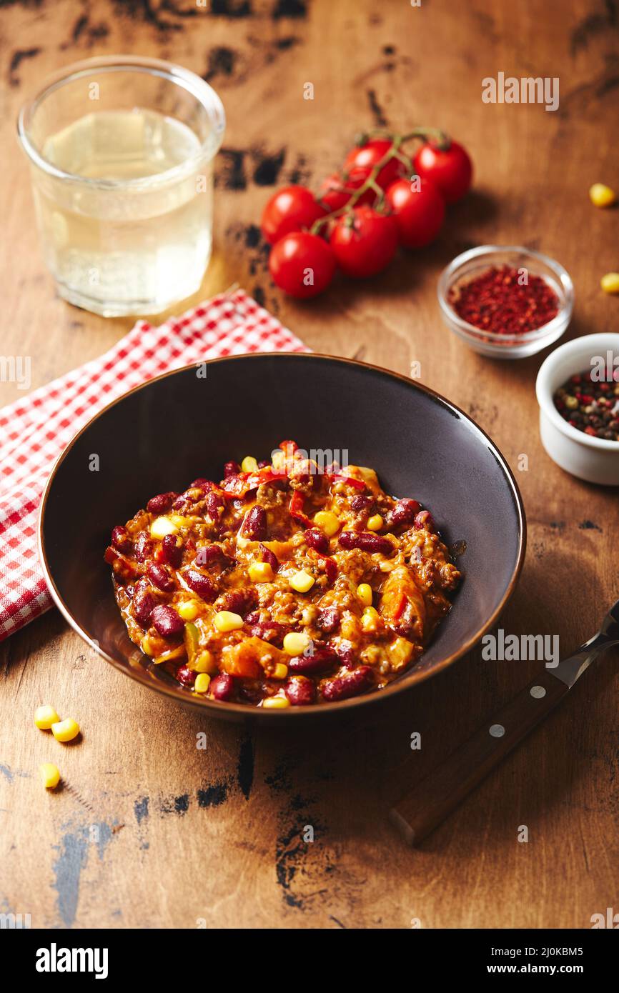 Chili Con Carne with ground beef, beans and corn in dark bowl on wooden ...