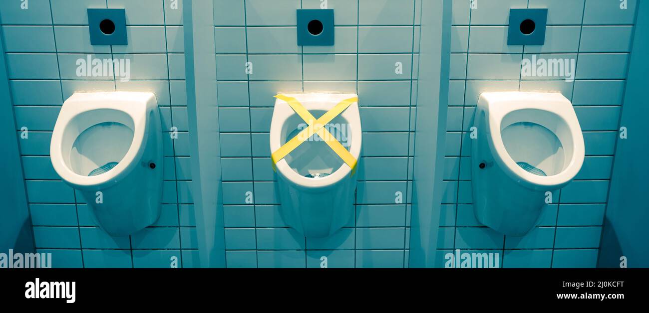 Urinal closed with yellow protective tape for social distance reason