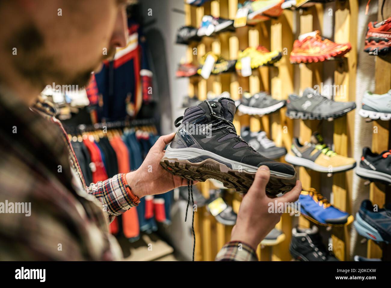 Caucasian man chooses and measures hiking boots at a sports and travel store. Man looking at hiking shoes in outdoor shop. Male Stock Photo