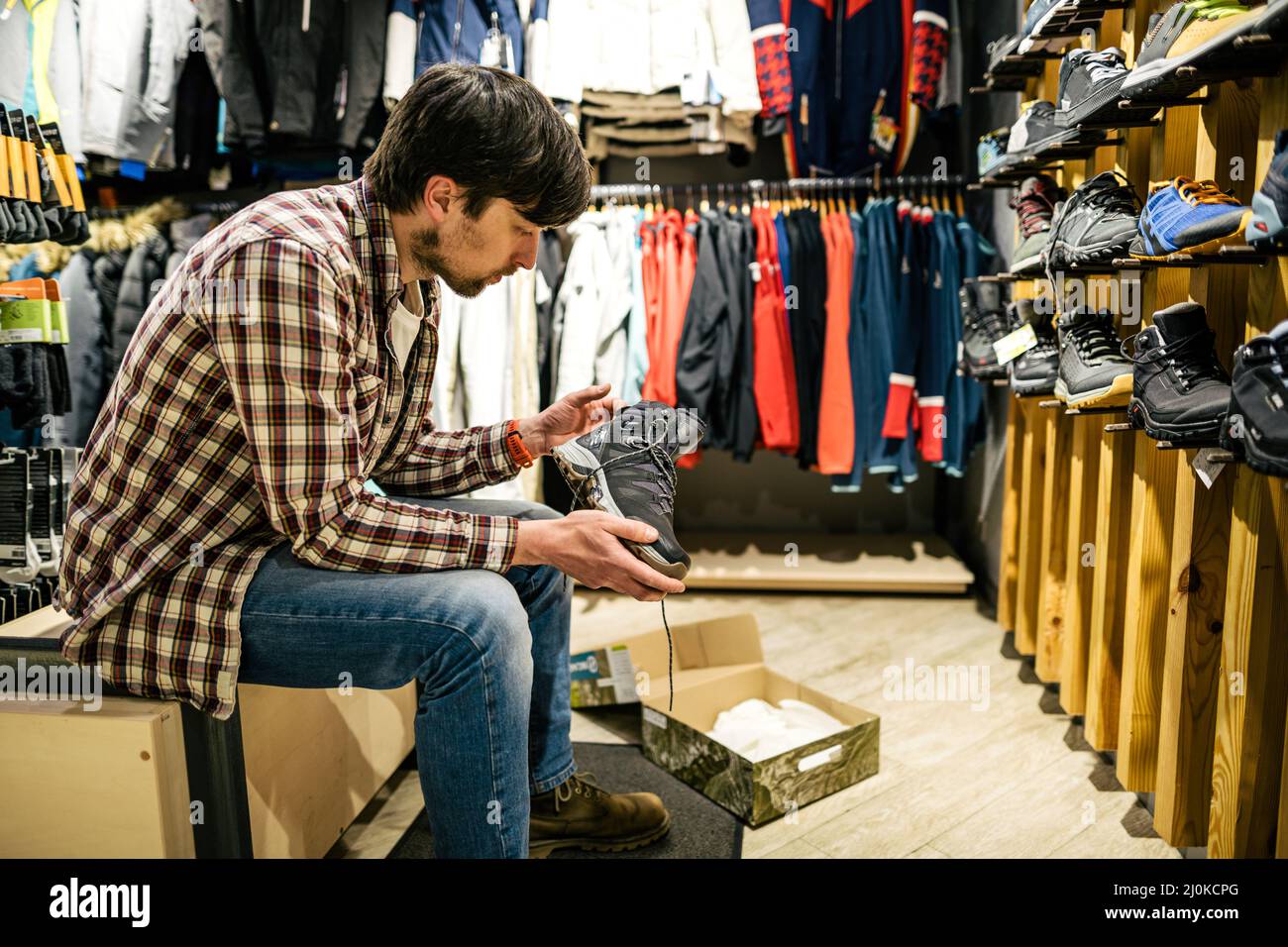 Man shopping in an outdoor store. Male buying mountain boots. Shopper in sports store select hiking shoes. Customer purchase of Stock Photo
