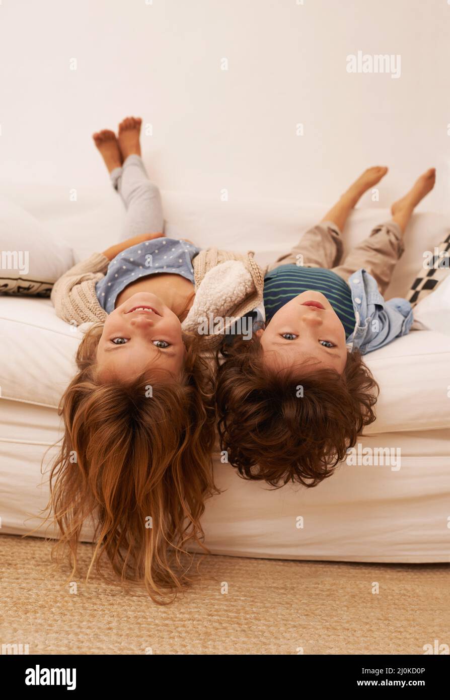 Even upside down were still bored. Portrait of two young children lying on a sofa with their heads hanging over the edge. Stock Photo