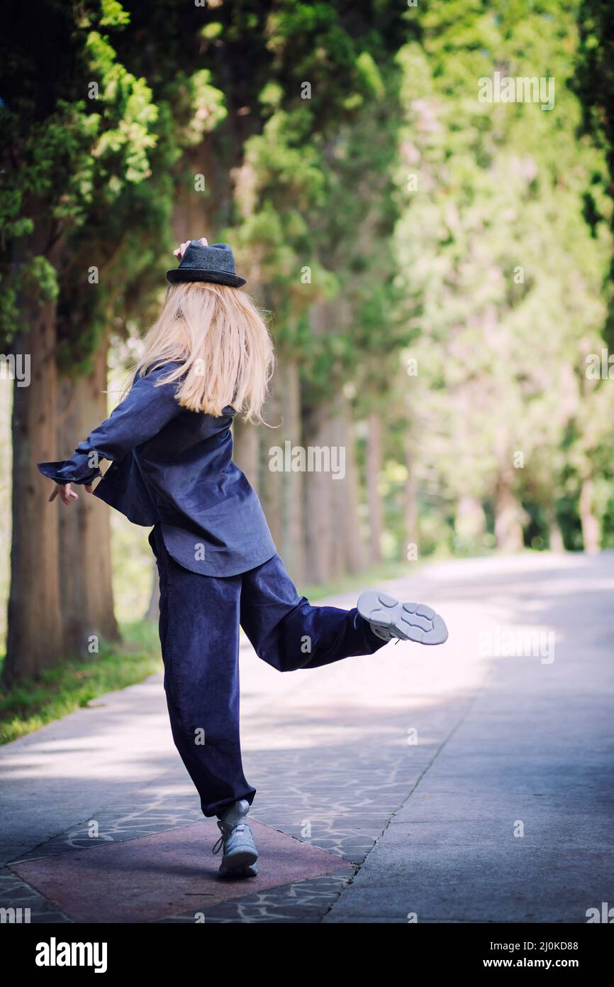 Woman in blue clothes and a hat in a dancing pose on an alley in the park. Street dancer Stock Photo