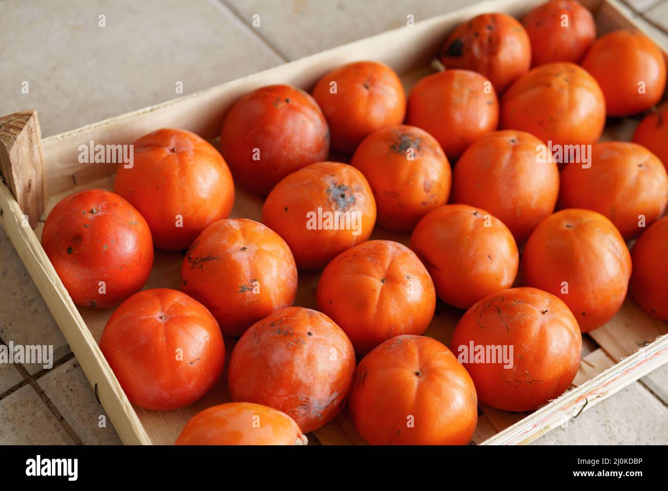 Ripe orange persimmons in a drawer. The texture of the background is ...
