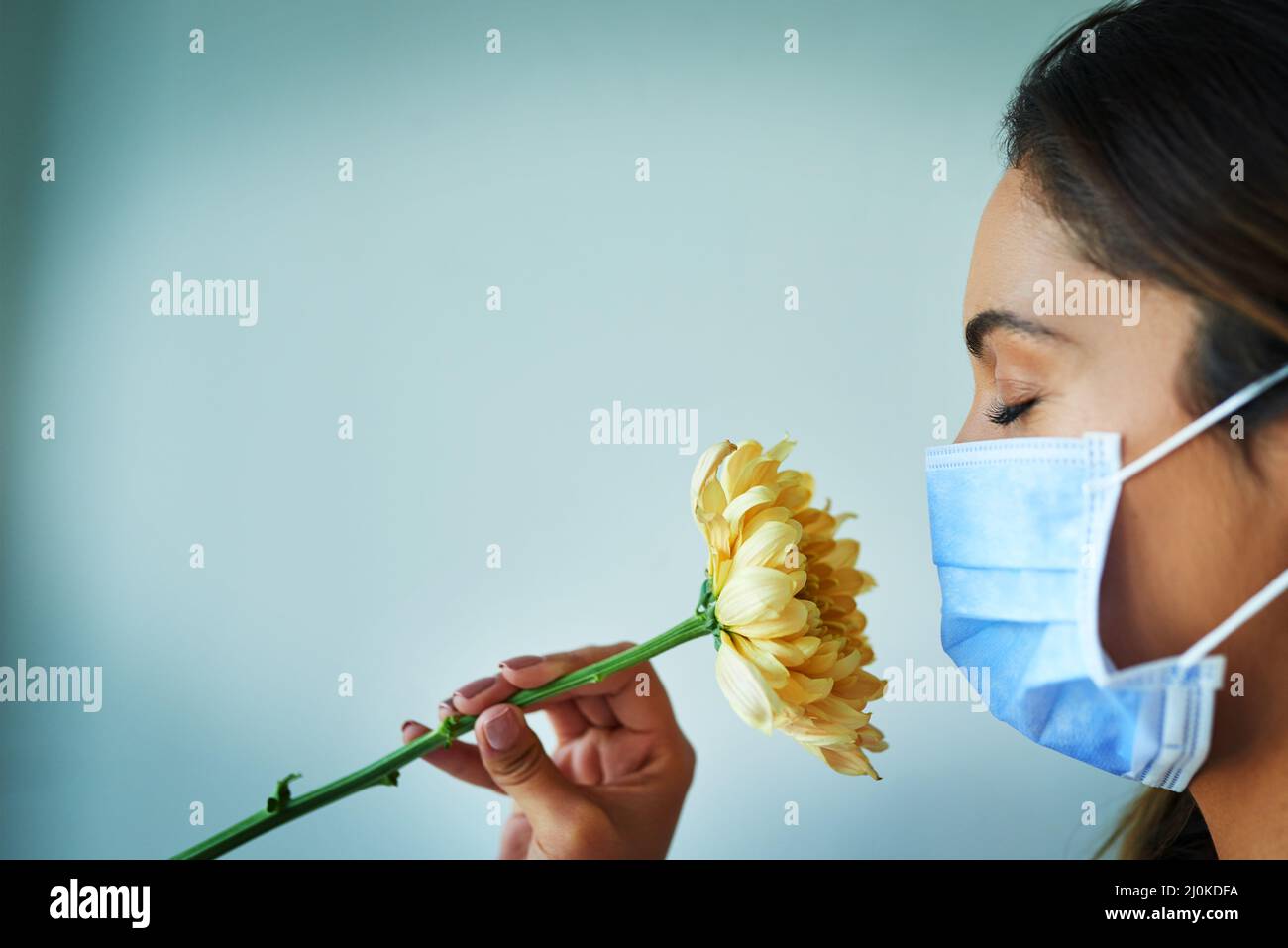 I cant seem to smell anything. Shot of a young woman smelling a flower while wearing a surgical