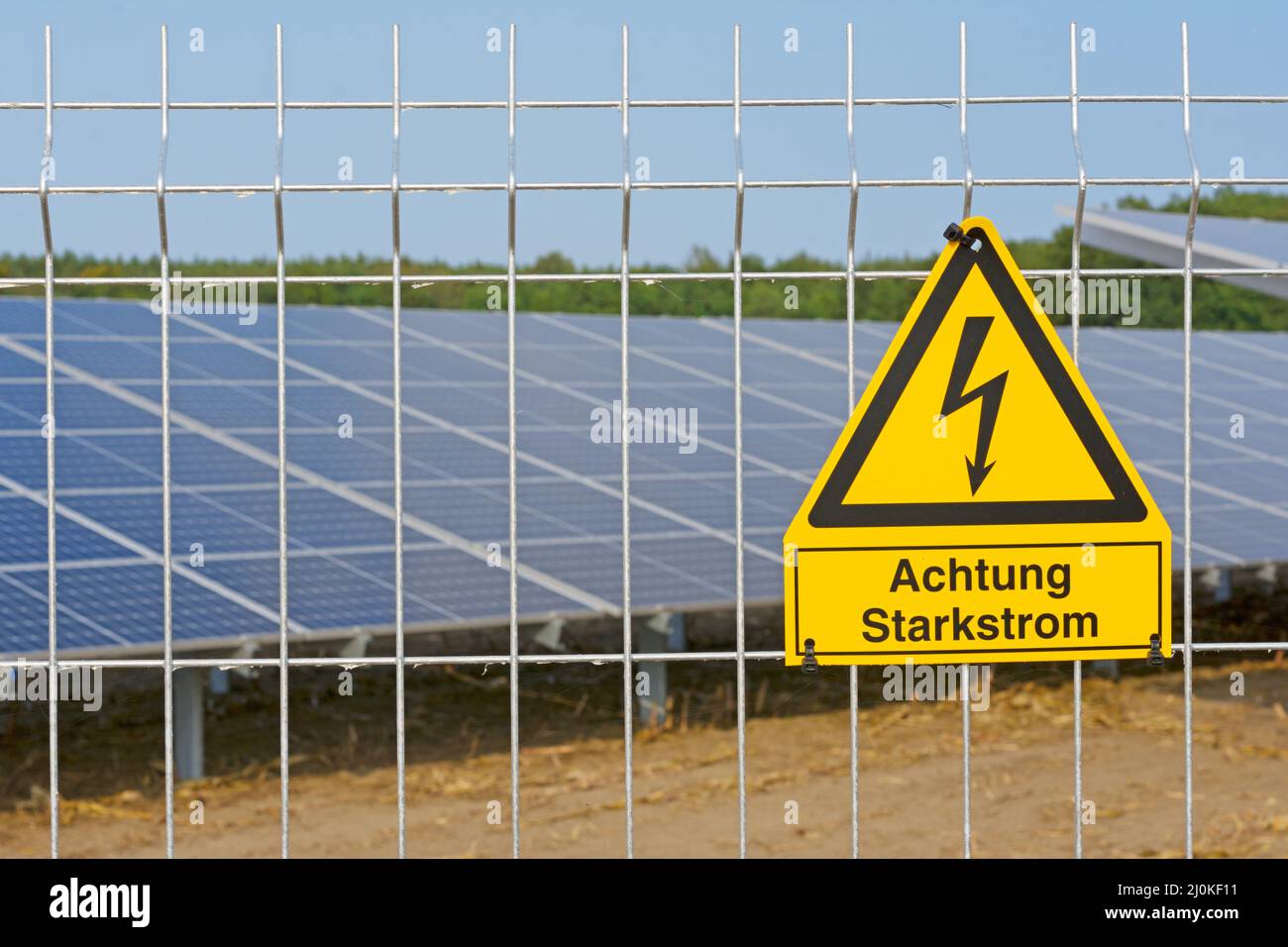 German warning sign Achtung Hochspannung (Attention high voltage) in front of solar system. Stock Photo