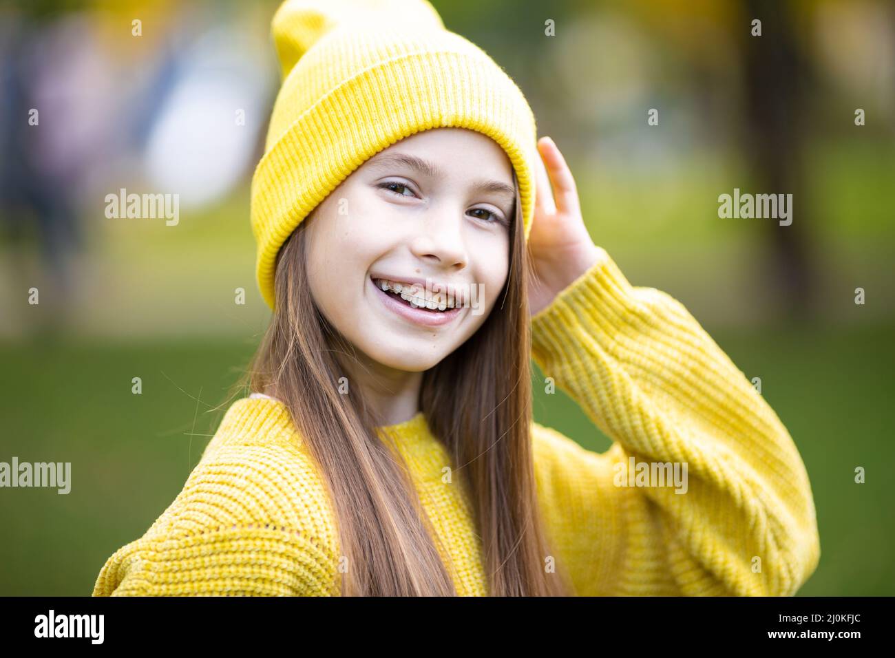 Portrait of modern happy teen girl with dental braces dressed in yellow clothes in park. Pretty teenage girl wearing braces smil Stock Photo