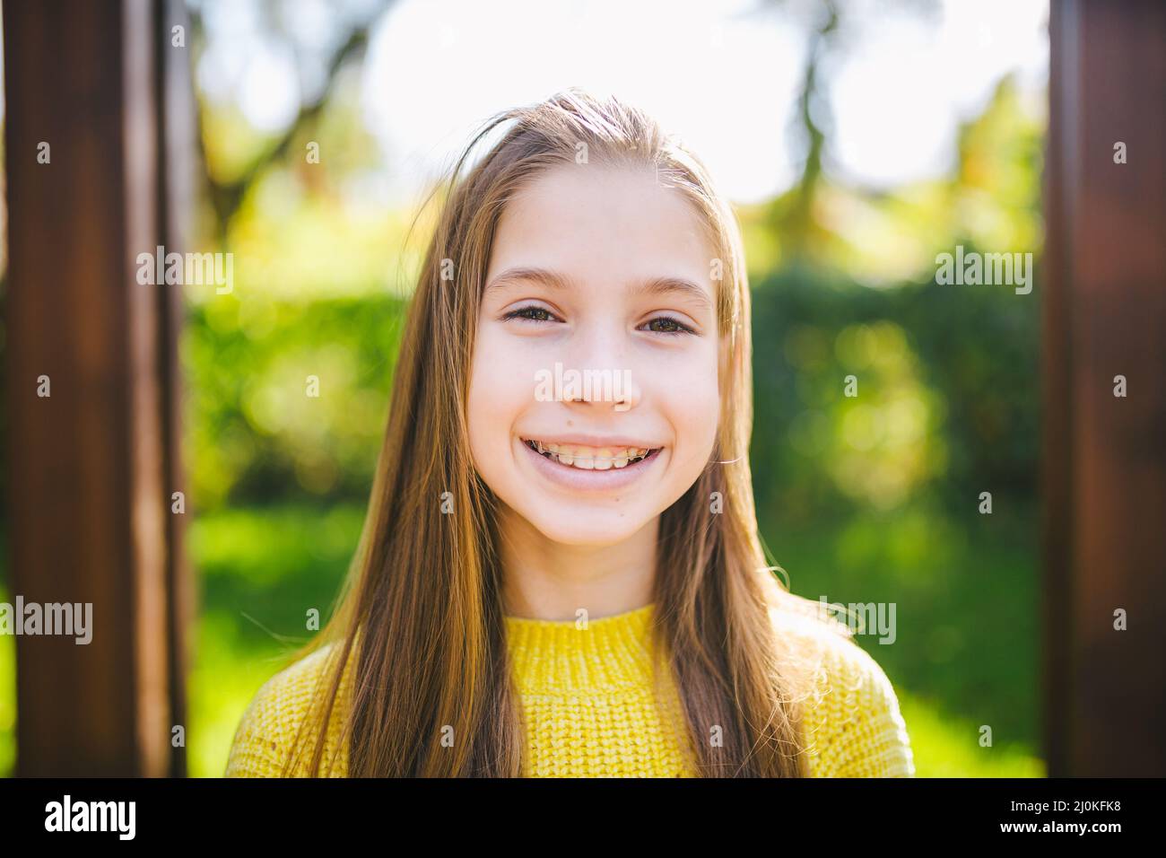 Portrait of modern happy teen girl with dental braces dressed in yellow clothes in park. Pretty teenage girl wearing braces smil Stock Photo