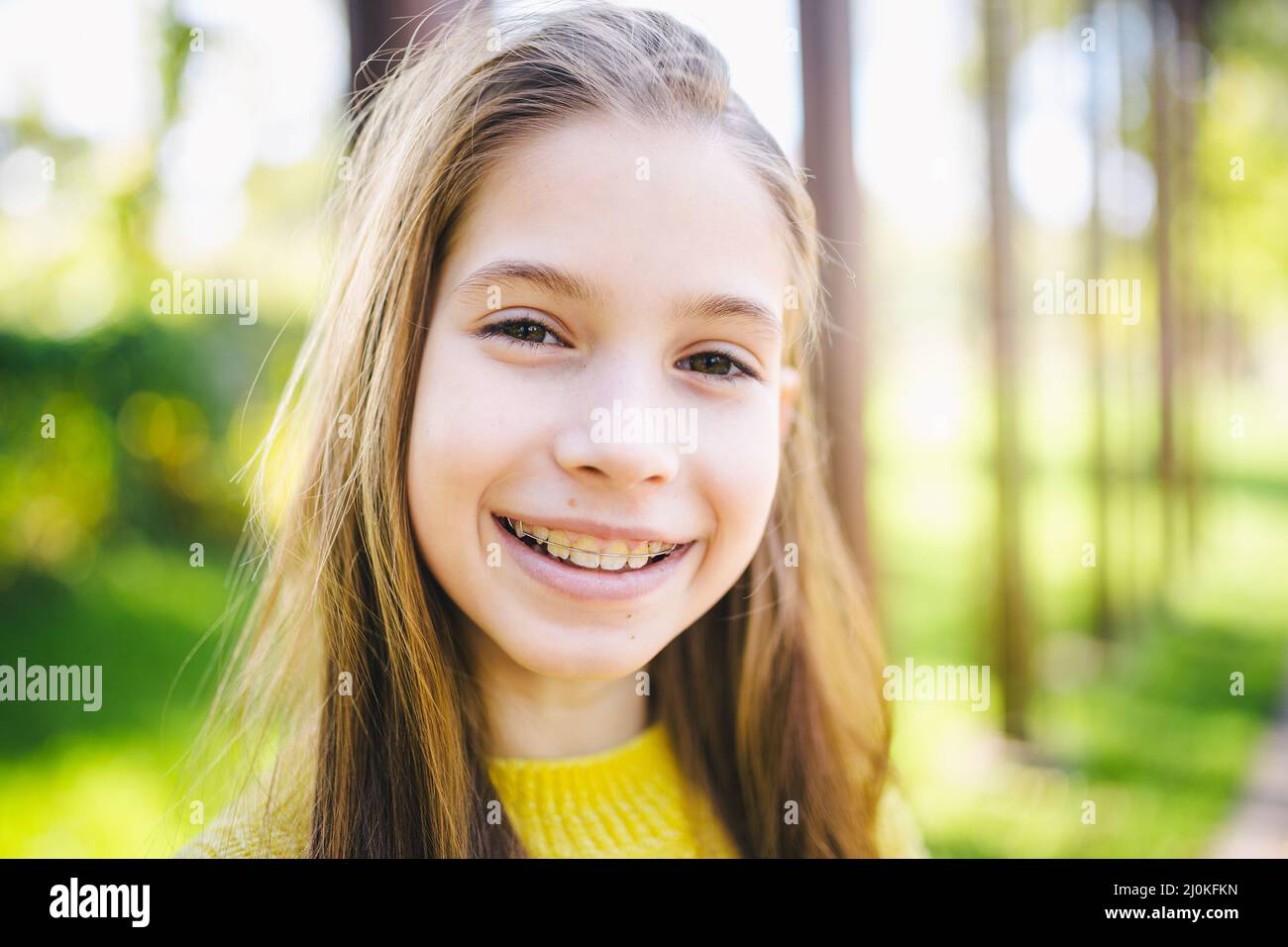 Pretty teenage girl wearing braces smiling cheerfully dressed in bright yellow clothes outdoors. Cute and happy teen girl with b Stock Photo