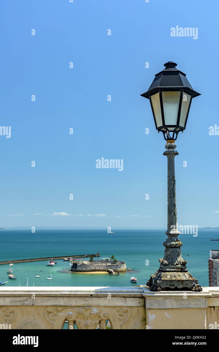 Old lamppost on a wall overlooking the sea and historic fortification in Salvador city Stock Photo