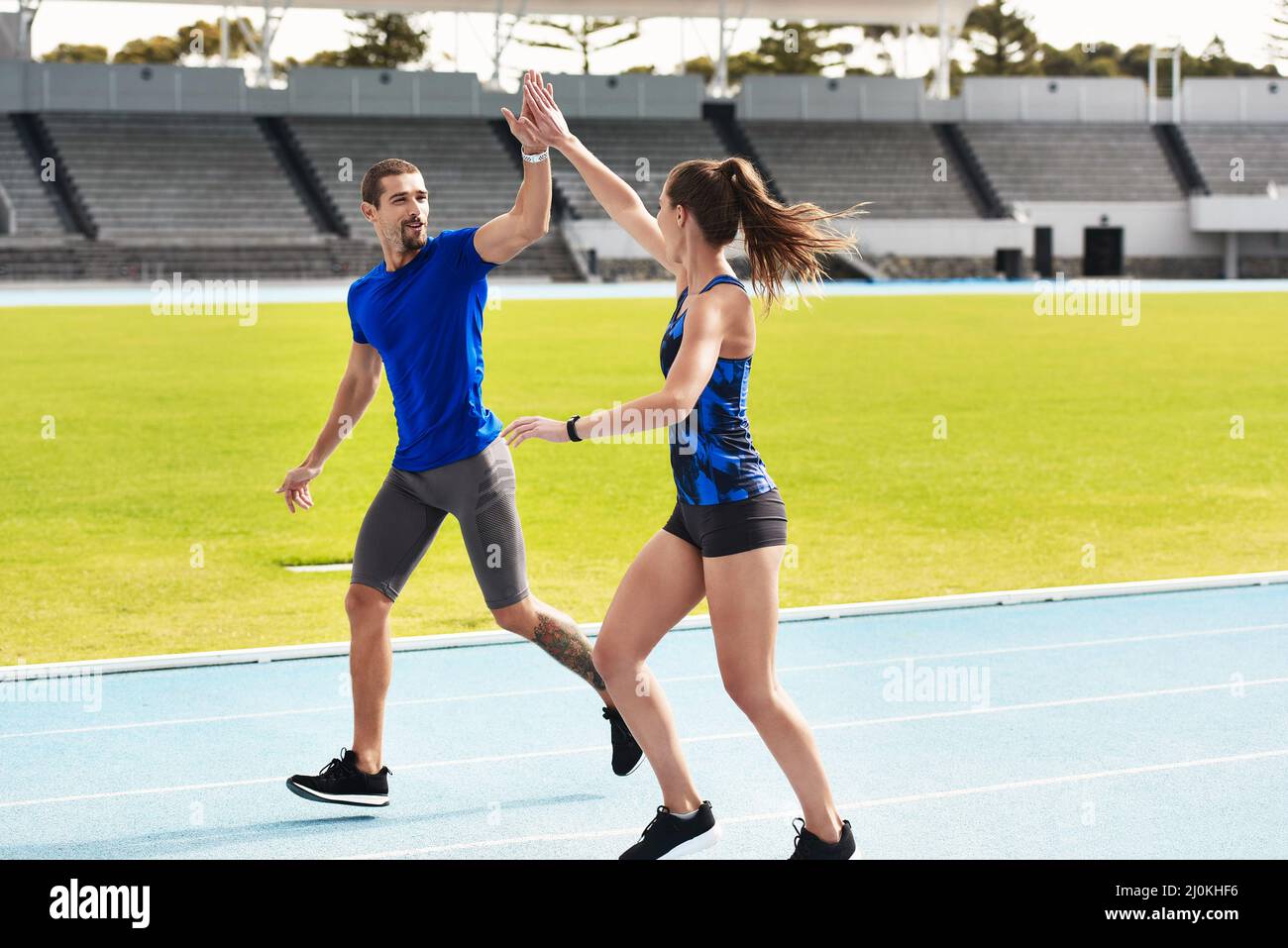 Good job. Full length shot of two young athletes high fiving while running along the track. Stock Photo