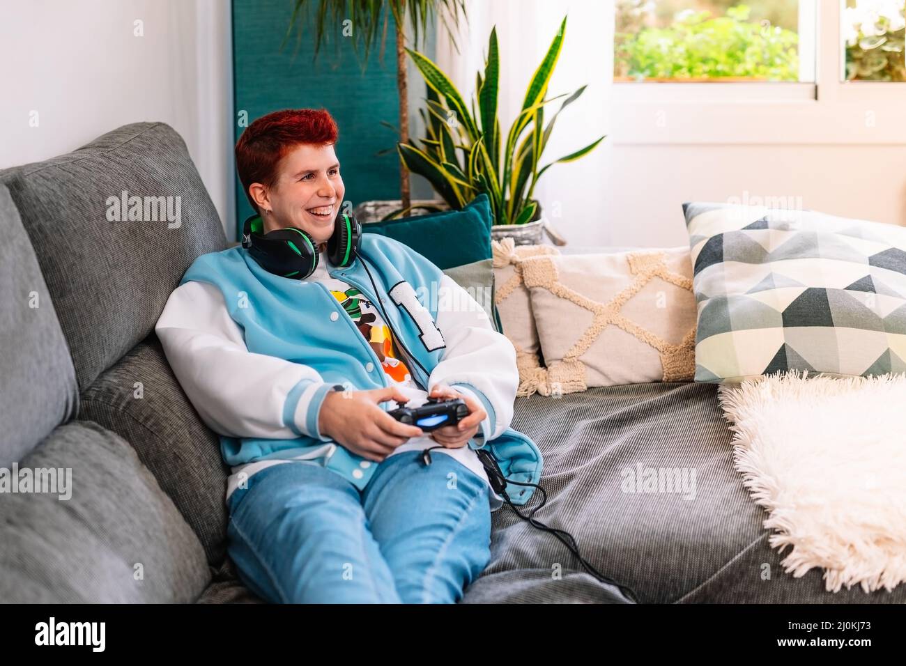 Non-binary smiling person playing video games in the living room at home Stock Photo