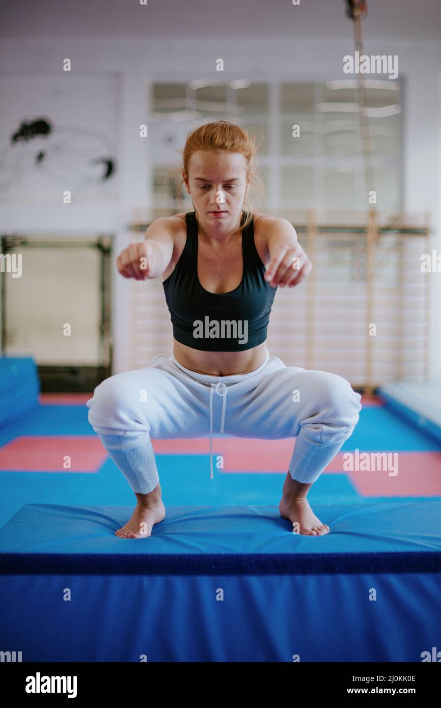 The young strong woman landed on a mat in the squat and her hand is outstretched in front of her Stock Photo