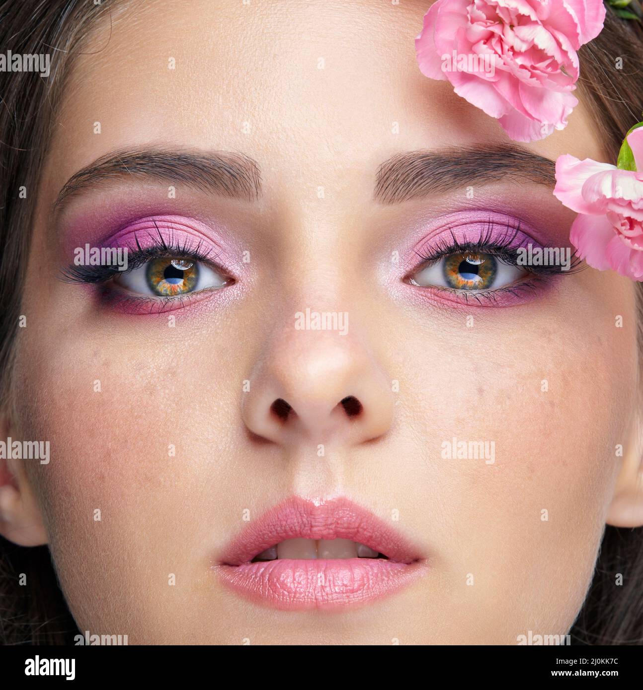Closeup portrait of female face with pink beauty makeup and carnation flowers on the temple. Stock Photo