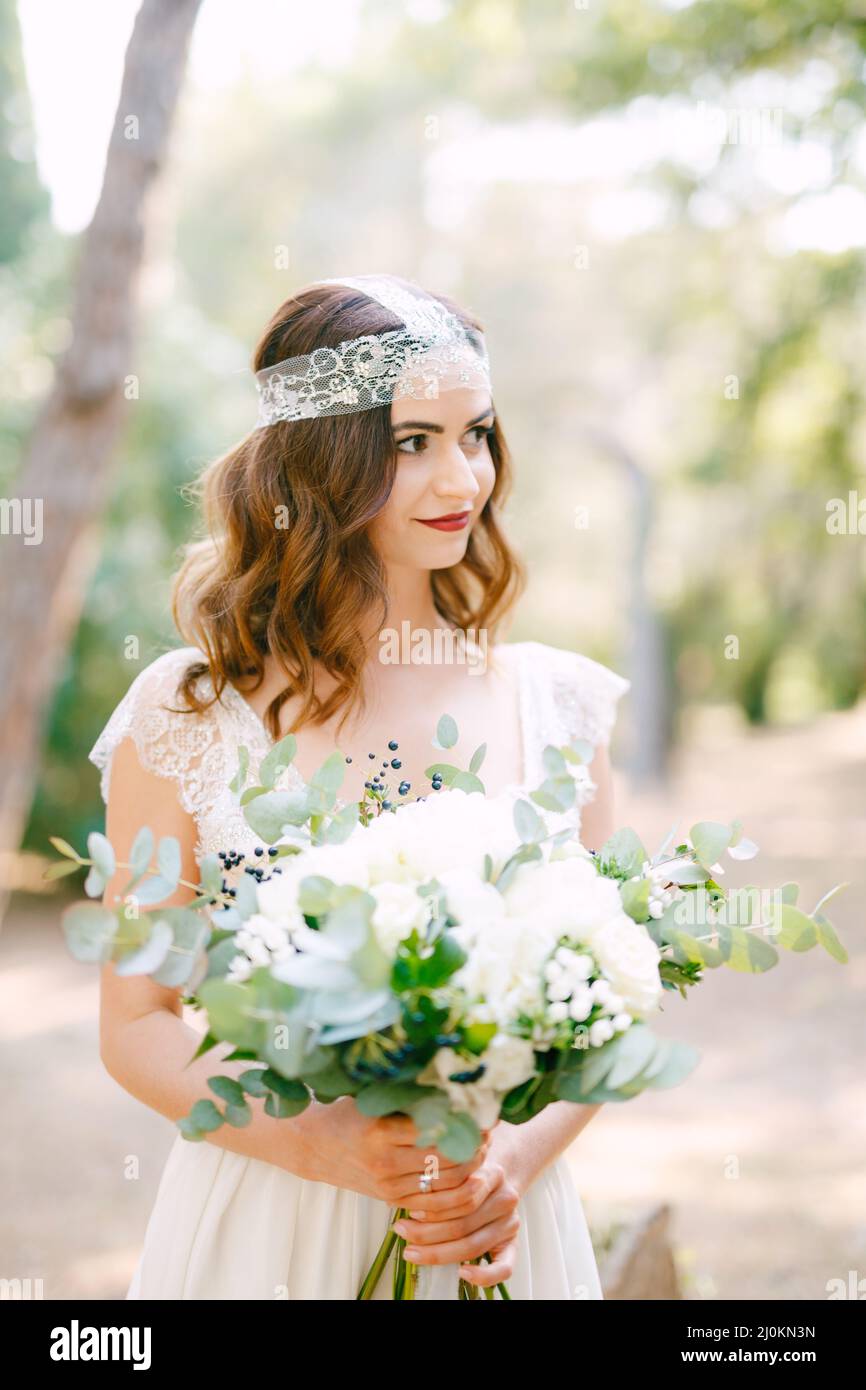 The bride is holding a wedding bouquet of roses, eucalyptus branches, delicate white flowers and dark berries in her hands Stock Photo