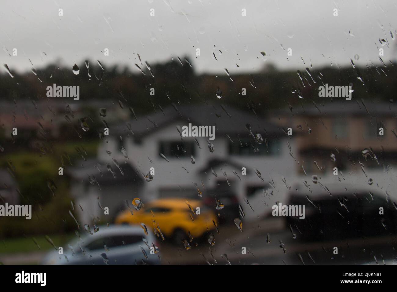 Auckland suburb, Waiake Beach, New Zealand - May 31 2020: the view of rain drops on a window with blurred city background with residential buildings a Stock Photo