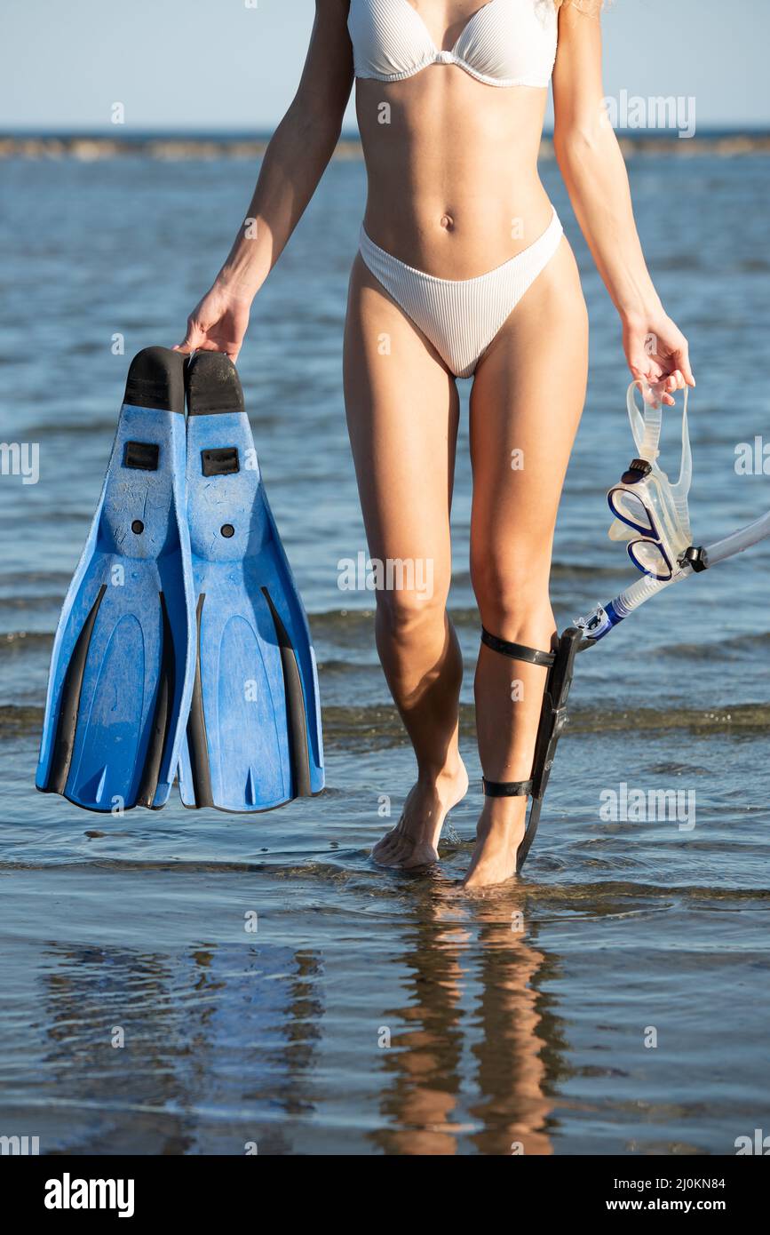 Young unrecognized woman wearing a white summer swimsuit and holding diving equipment at the beach Stock Photo