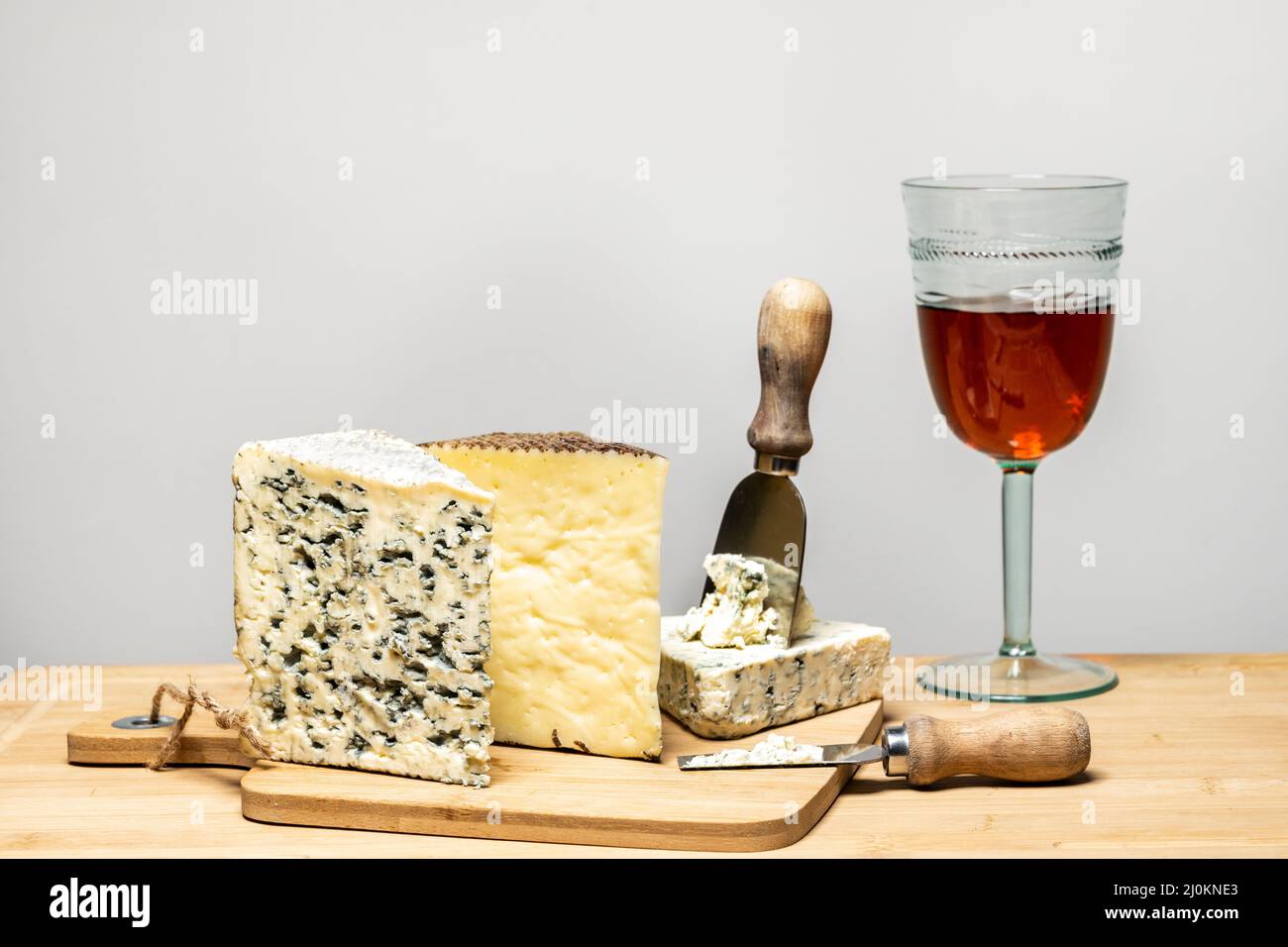 Delicious cheese wedges of different varieties with specialized cheese knives and a glass of Spanish wine on a cutting board eaten in turn on top of a Stock Photo