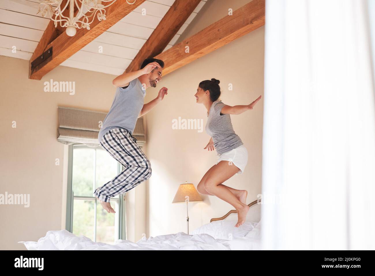 We bring a world of fun into each others lives. Full length shot of a cheerful young couple playing and jumping on their bed in their bedroom at home. Stock Photo