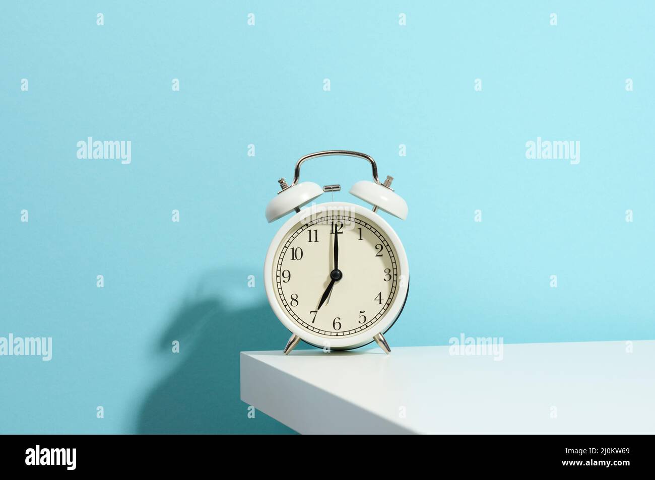 Round white alarm clock on the table. Time seven in the morning, get up early, change hours Stock Photo