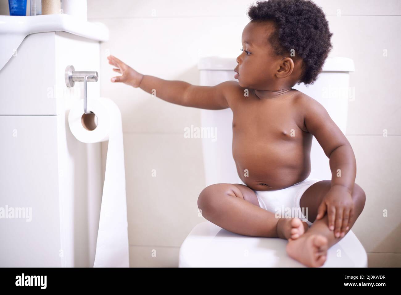 Potty training 101 Always make sure you have enough toilet paper. Shot of a baby boy sitting on the toilet and reaching for the toilet paper. Stock Photo