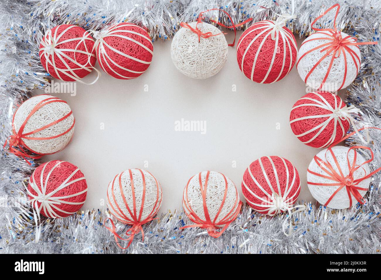Shiny silver tinsel with white and red Christmas balls borders a blank white background. Top view Stock Photo