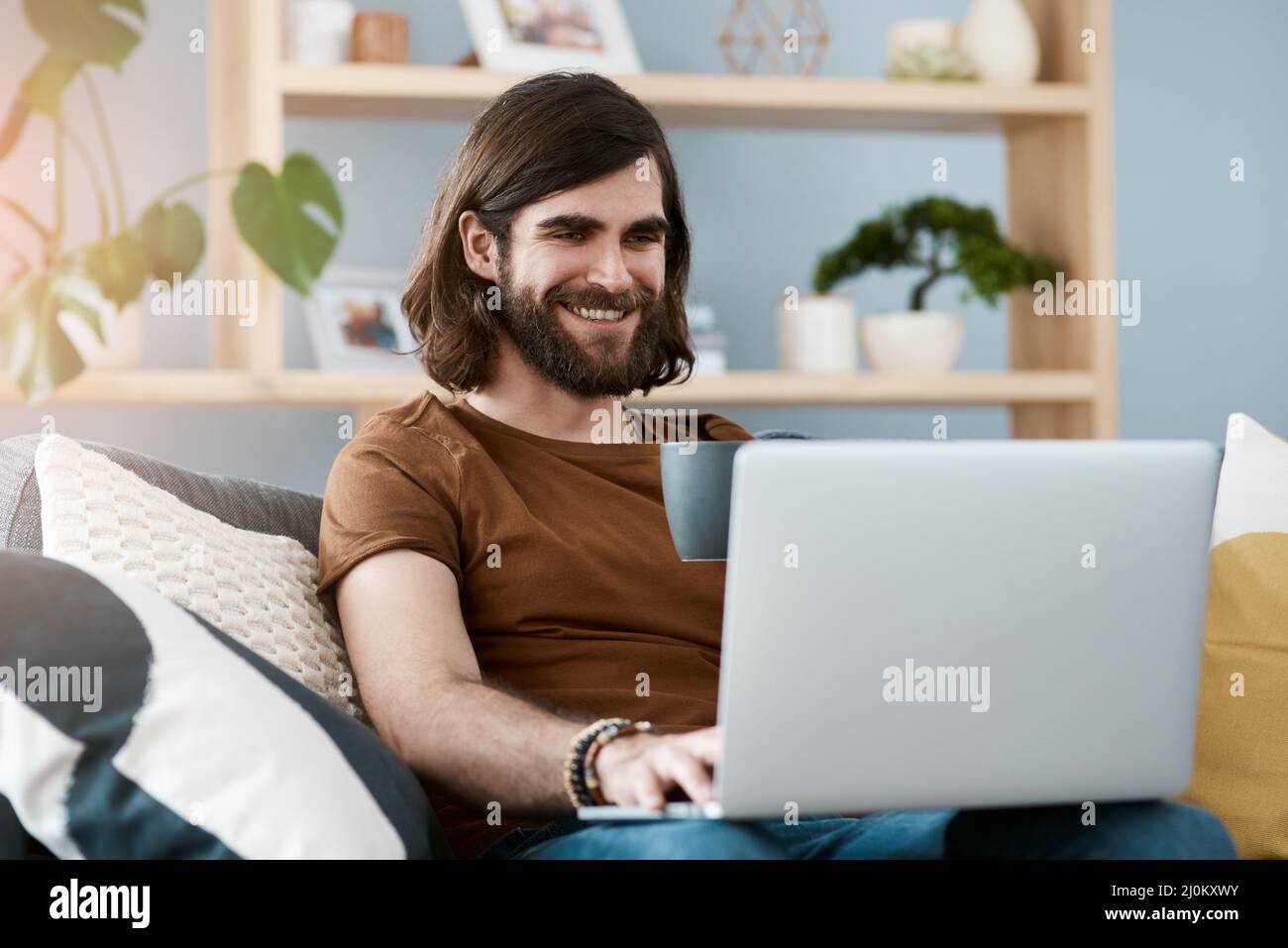 Hes in a good mood today. Shot of a handsome young man using his laptop while relaxing on a sofa in his living room. Stock Photo