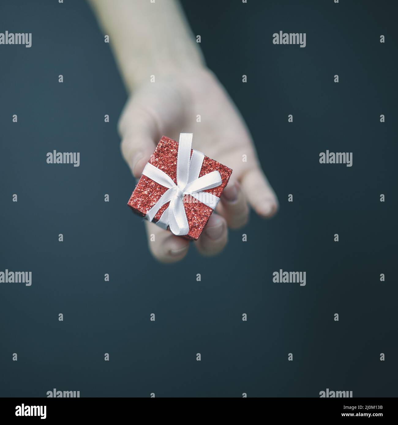A tiny shiny red box with a white bow lies in women's fingers Stock Photo