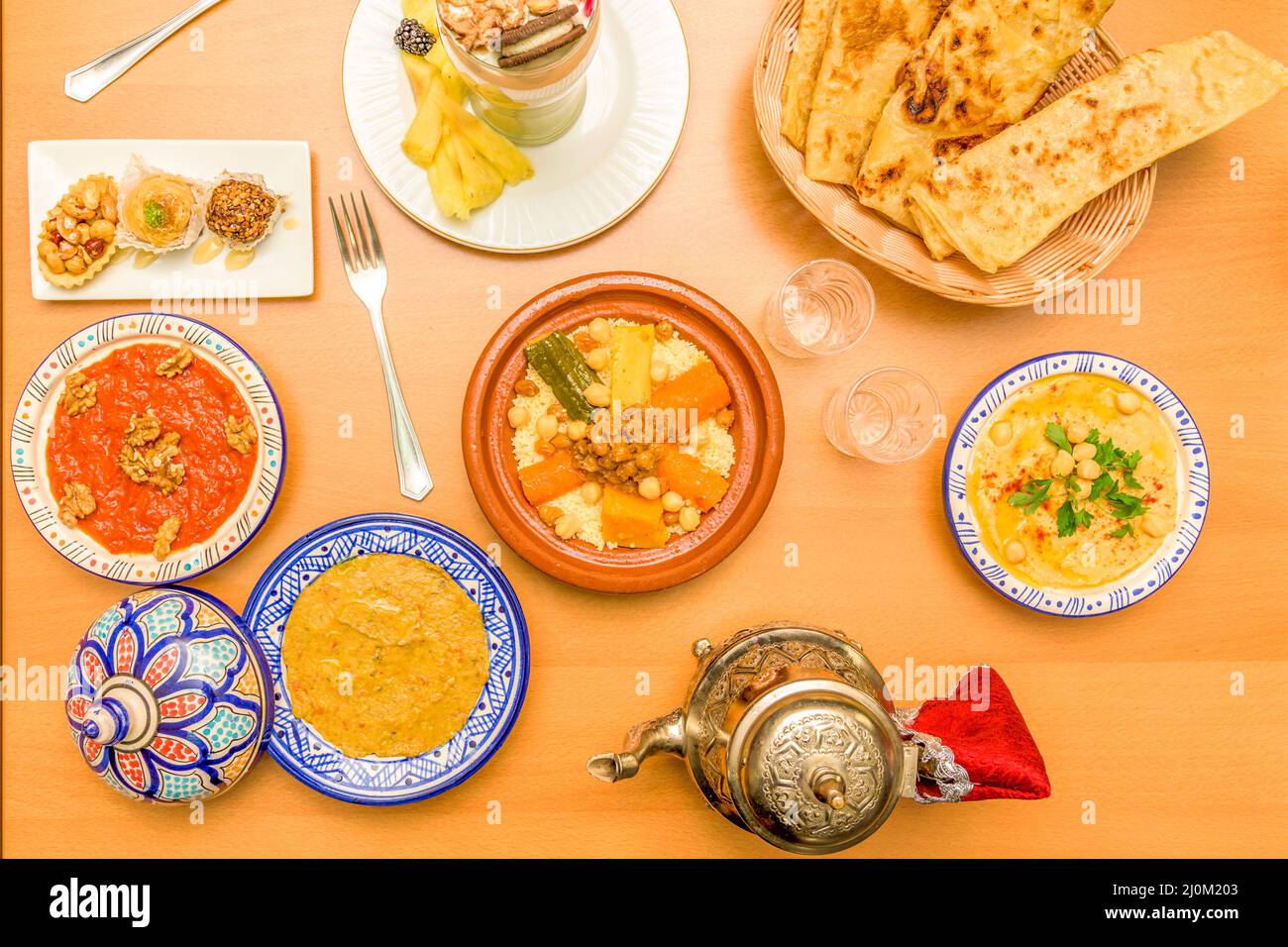 Colorful Moroccan food plates with couscous, lamb tagine, baklava, hummus and smoothies Stock Photo