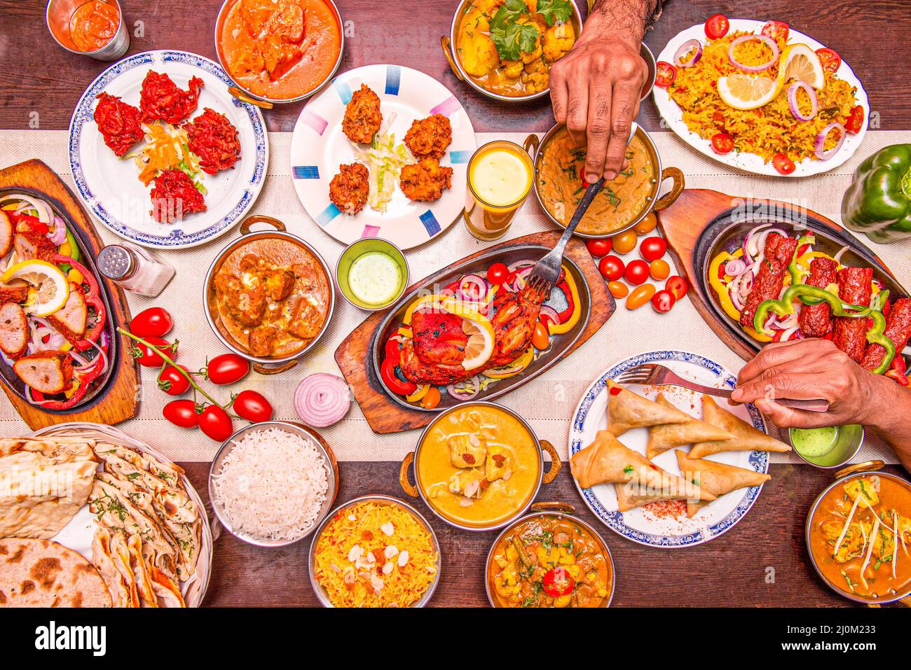 Set of Indian food dishes with hands poking the chicken tikka masala, another on the stuffed samosas and curry Stock Photo