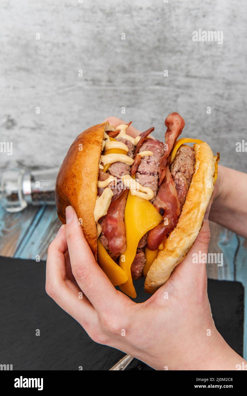 holding in two hands a monster trimeat beef burger with lots of fried