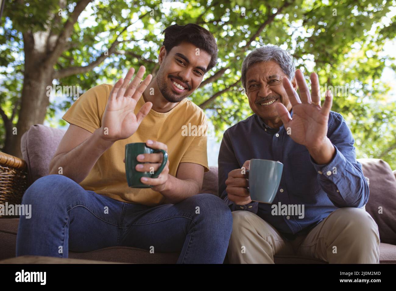 Happy biracial adult son and senior father holding cups of coffee and making laptop video call Stock Photo
