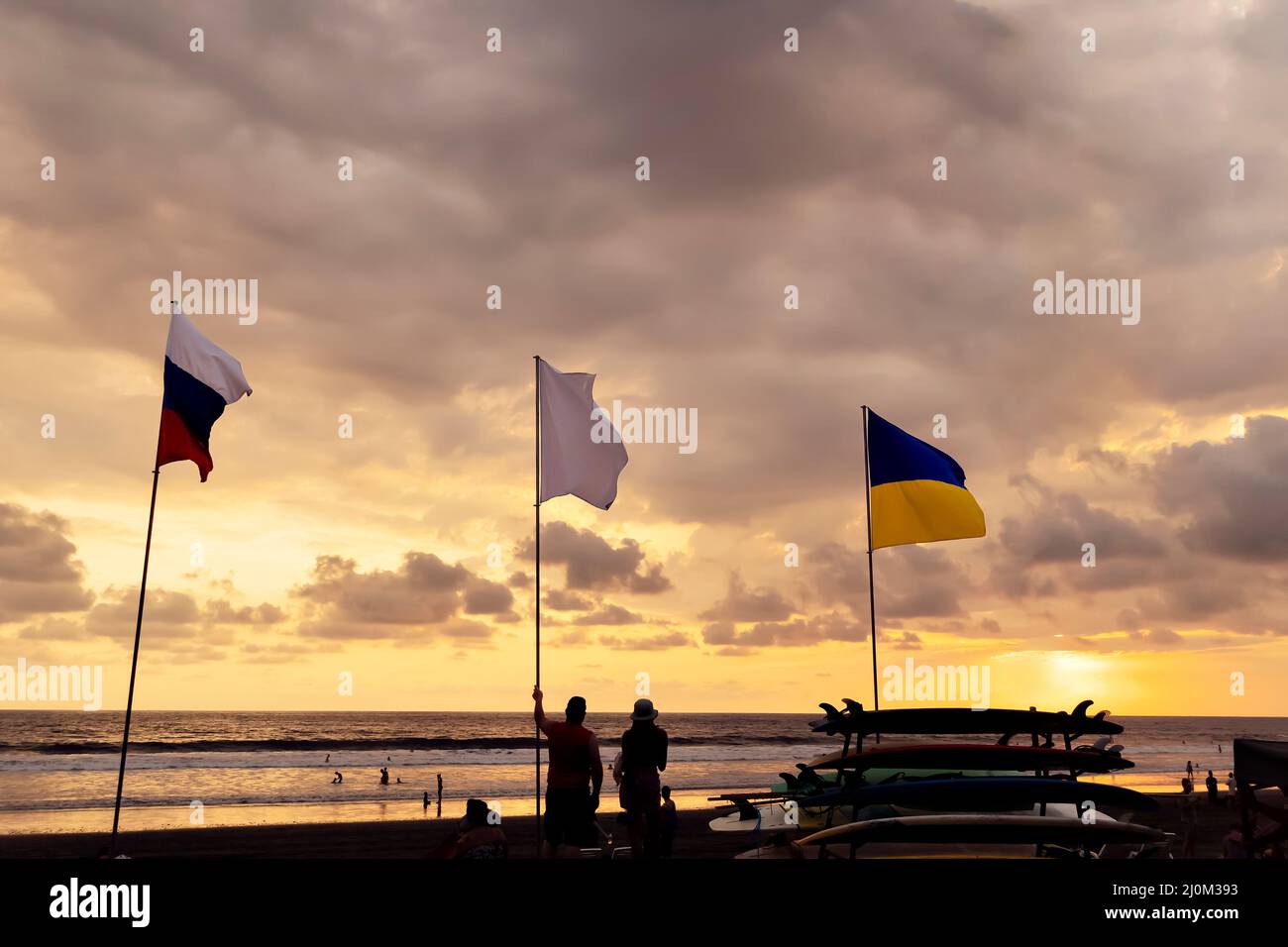 Ukrainian and Russian flags on sky background at sunset on the beach. Stock Photo