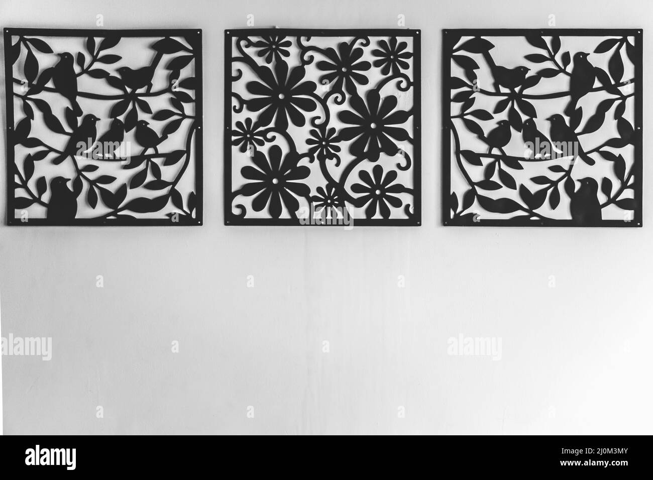 Black metal cut decoration frame hanging on the white wall. Ornamental laser cut birds and