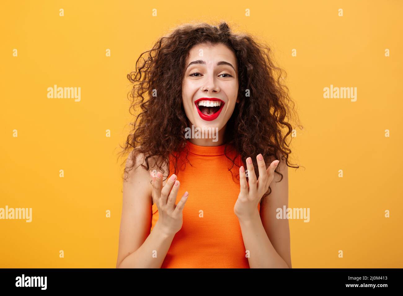 Surprised thrilled and joyful charming european female with curly hairstyle raising palms in grateful and delighted gesture smil Stock Photo
