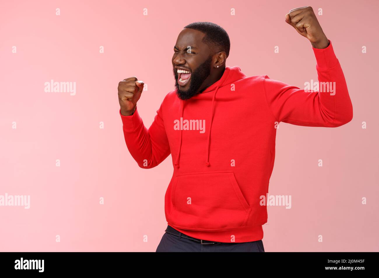 Extremely happy bearded young 25s black guy triumphing happily yelling yeah raising clenched fists celebrating success winning b Stock Photo