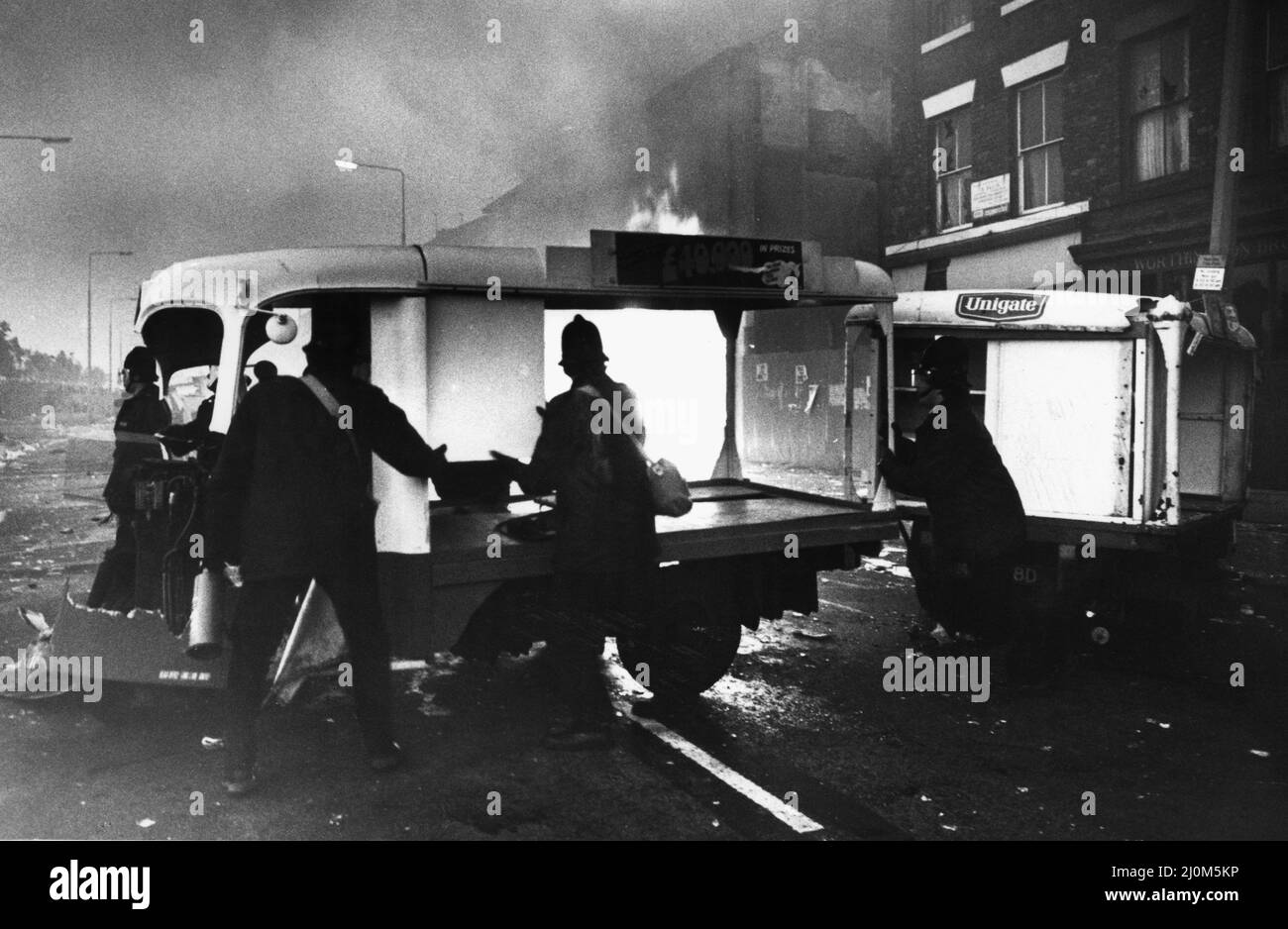 Toxteth Riot 6th July 1981Police officers try to clear a road block of milk floats on Park Road so the fire brigade can control the fire raging in looted shops further up the road.. The riots was sparked following the interception by police of motorcyclists Leroy Cooper in Selbourne Street. A crowd gathered, name-calling grew into jostling and within minutes there was a full-scale fracas that saw three police officers hurt and a young local man, arrested on assault charges. It did not stop there. Police mounted extra patrols in the area and early the following evening, July 4, they came under Stock Photo