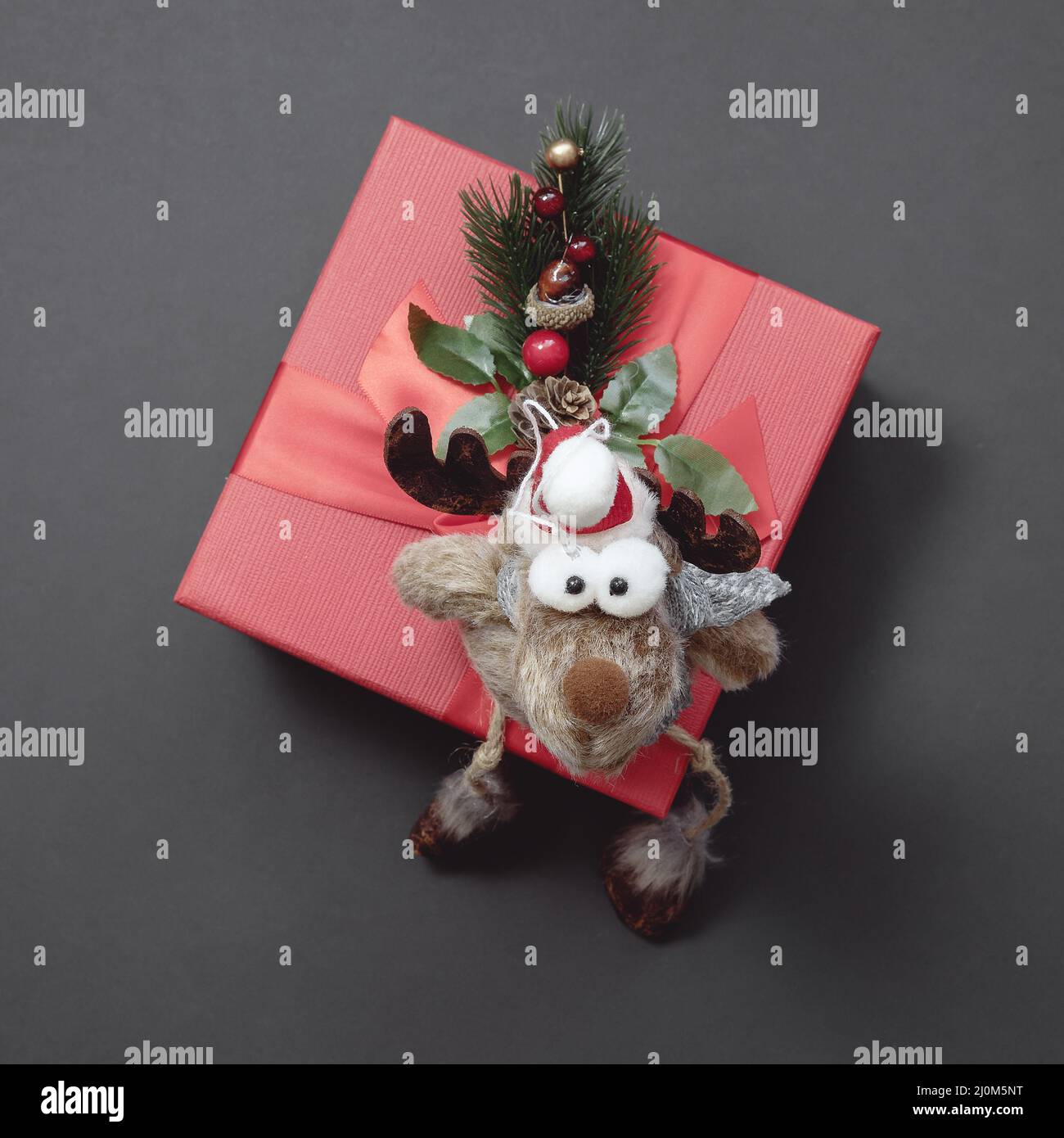 A funny soft toy deer sits on a red gift box decorated with a coniferous twig. Christmas composition Stock Photo