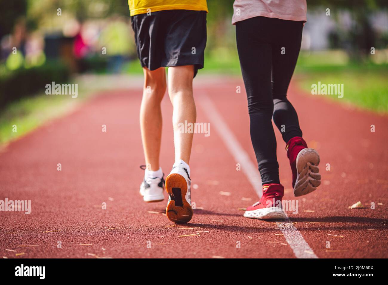 Four legs close-up brother and sister in sneakers run on red treadmill at running stadium back view. Two runners kids side by si Stock Photo