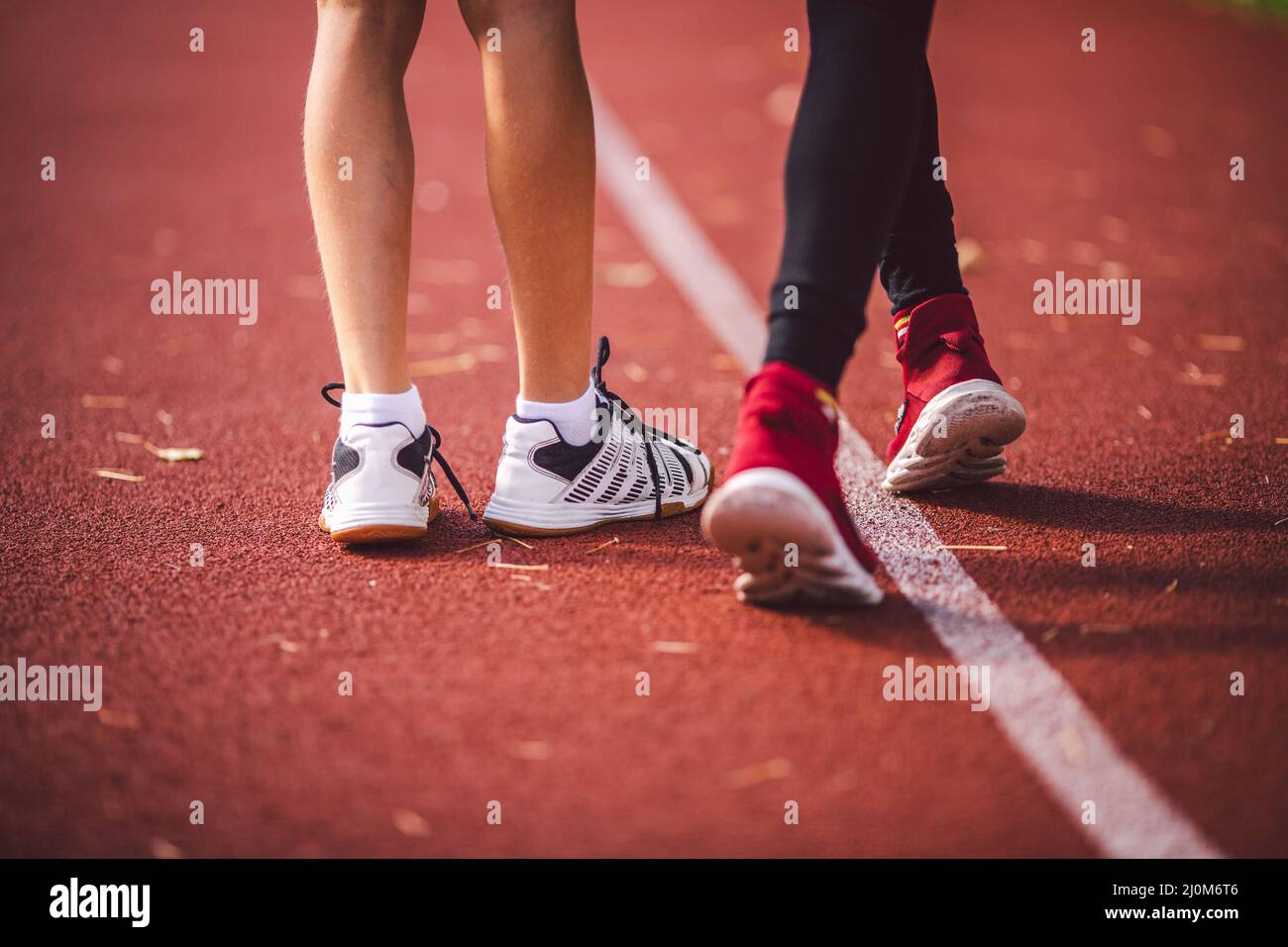 Four legs close-up brother and sister in sneakers run on red treadmill at running stadium back view. Two runners kids side by si Stock Photo