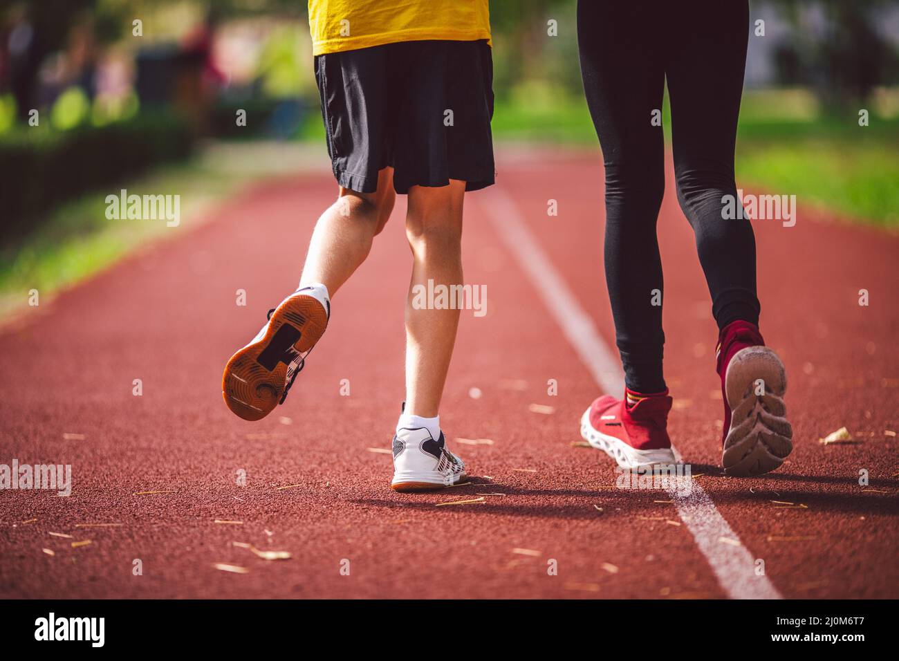 Close-up of legs in sneakers of two children on running track of stadium, back view. Boy and girl on red jogging track in park r Stock Photo