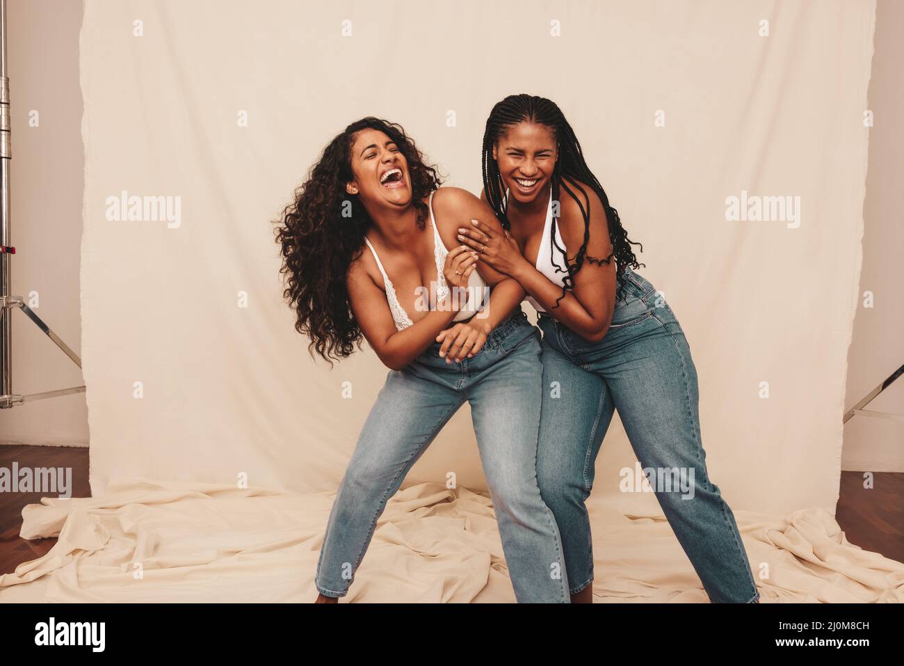 Fun in the studio. Two cheerful young women laughing and being playful while wearing denim jeans against a studio background. Two happy female friends Stock Photo