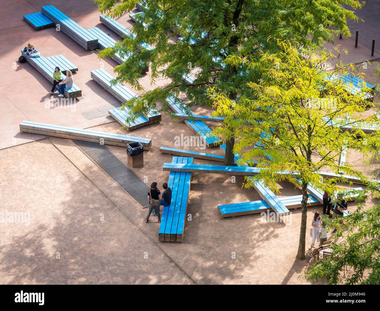 Linz Austria: Pattern of park benches under a tree with people resting and discussing overhead look Stock Photo