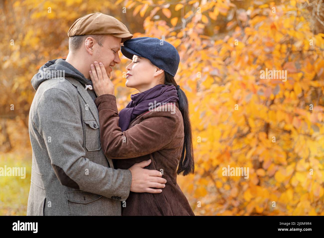 Caucasian Fall Couple Looking at Each Other's Eyes. Casual Couple in Stylish Caps in an Autumn Suburb. Close-up. Fall Background Stock Photo