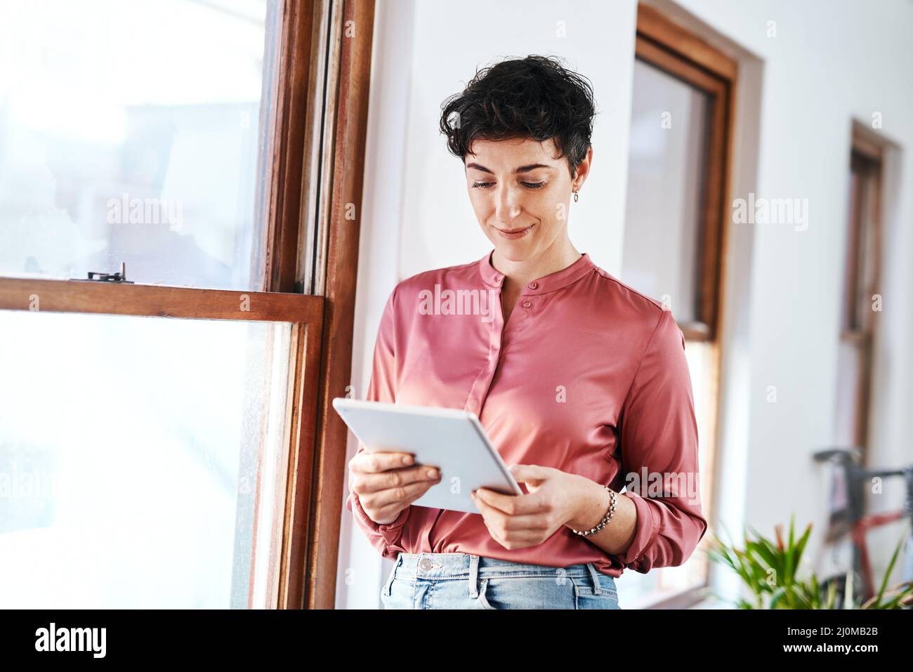 Checking company emails. Cropped shot of an attractive young businesswoman standing and using a tablet in her office alone. Stock Photo