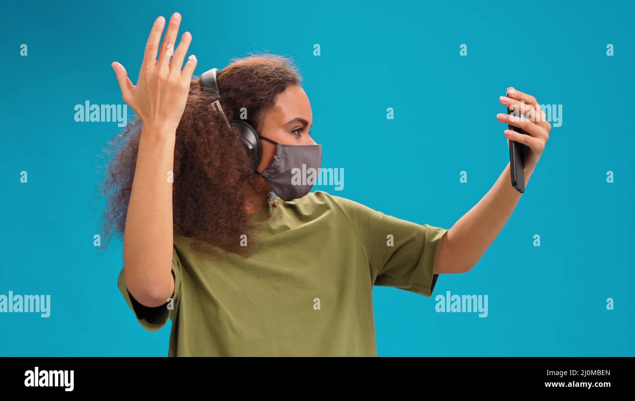 Making a video African American girl using her smartphone with headphones in olive t-shirt, reusable face mask, to prevent coron Stock Photo