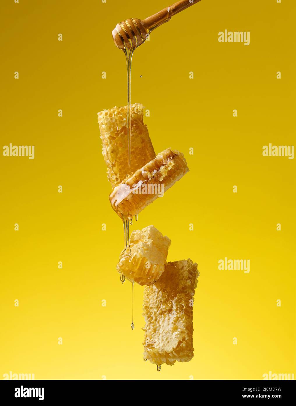 Pouring transparent sweet honey from a wooden stick on a wax honeycomb. Yellow background Stock Photo