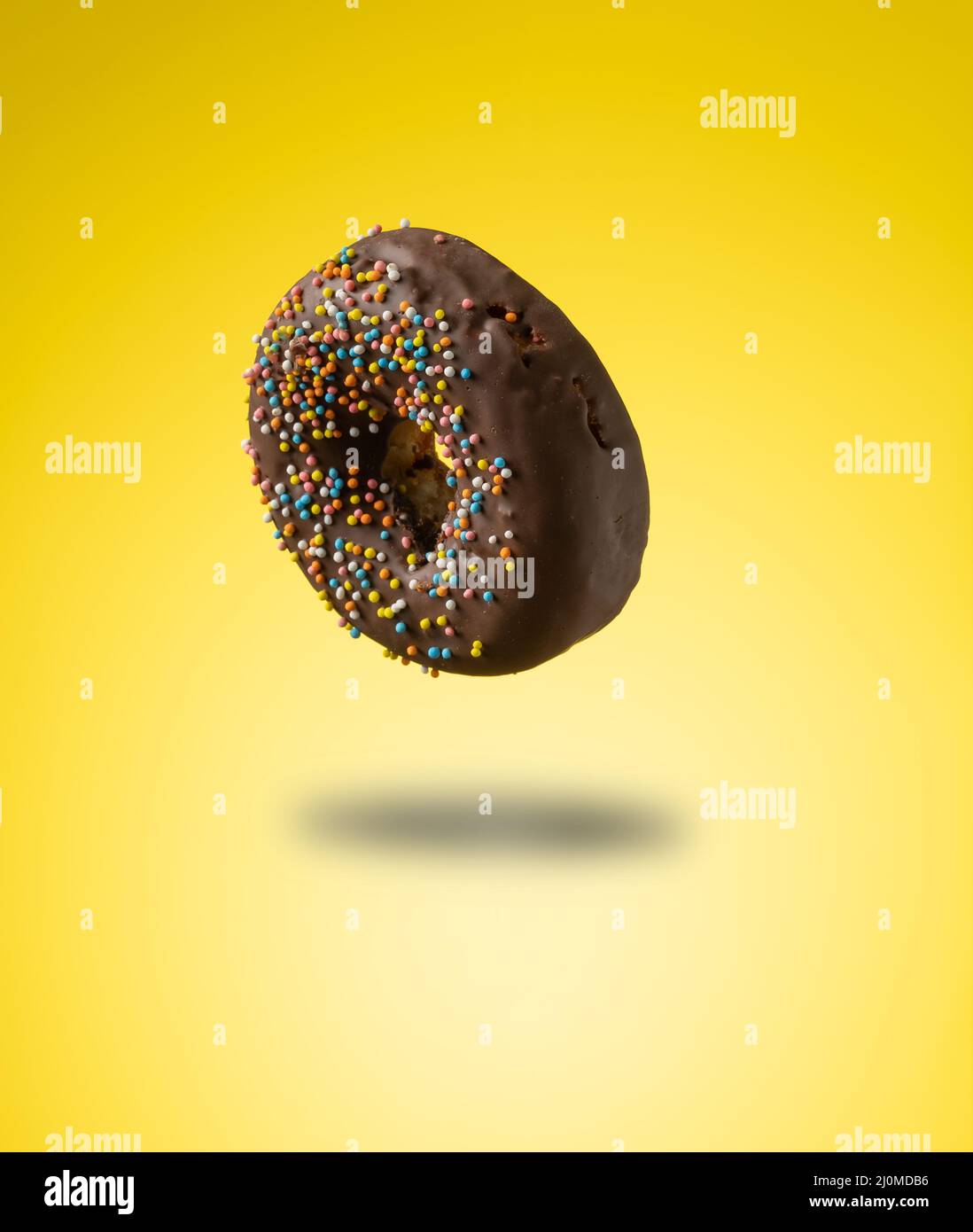 Chocolate donuts with multicolored sprinkles levitate on a yellow background Stock Photo