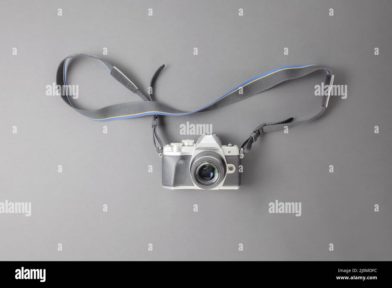 A retro camera with a strap lies on a gray background with the lens up. Top view Stock Photo