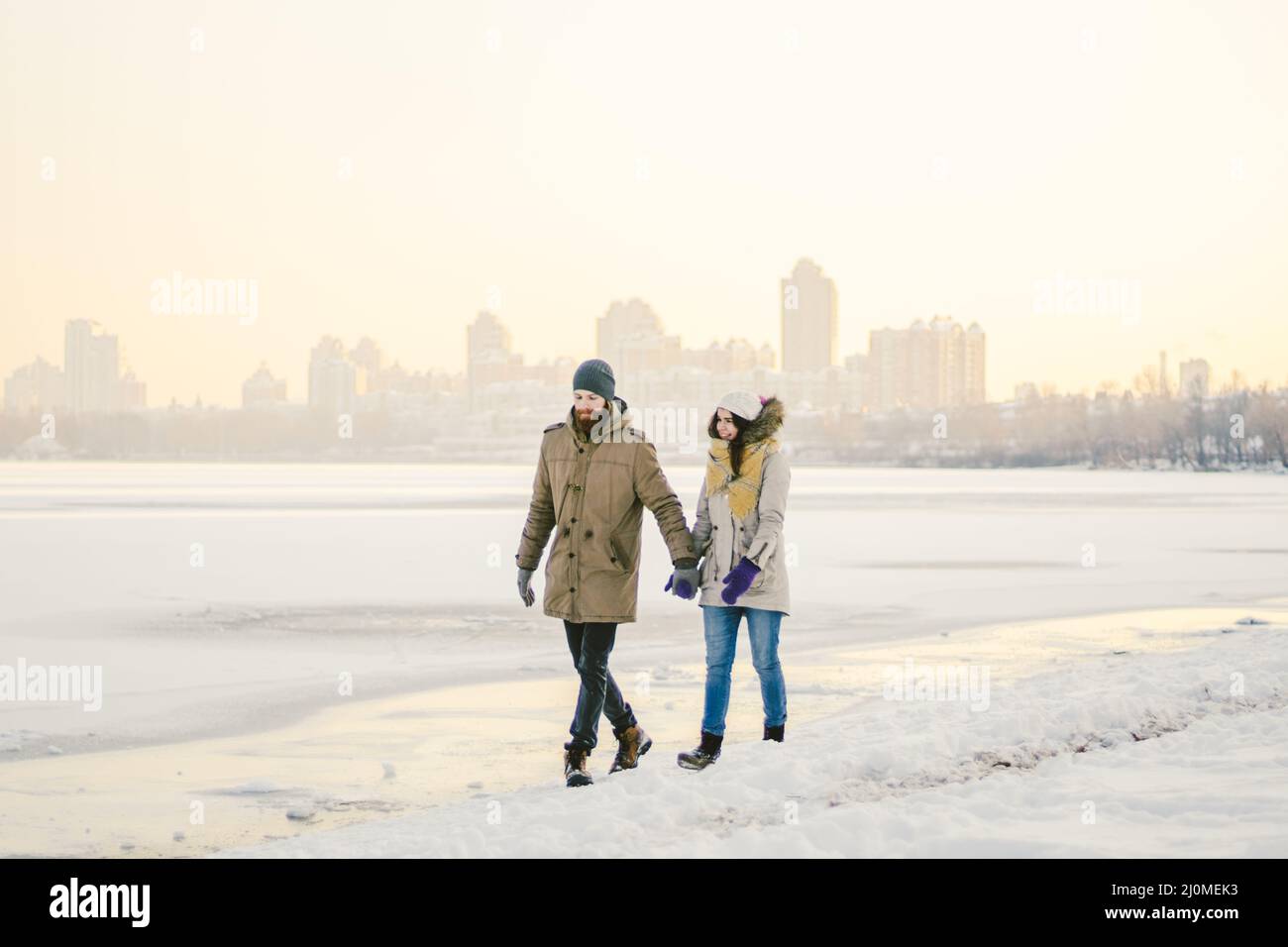 Theme Christmas holidays winter new year. Young stylish Caucasian loving couple Heteresexual walking on the shore of a frozen la Stock Photo