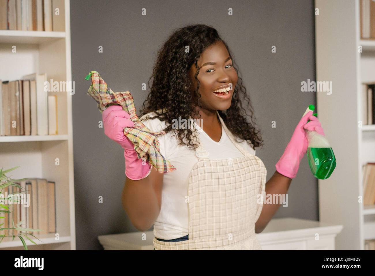 Afro American Girl in an Apron and Pink Rubber Gloves is Going to Do a Spring Cleaning in Her House. She Has Dust Cloth And Wind Stock Photo